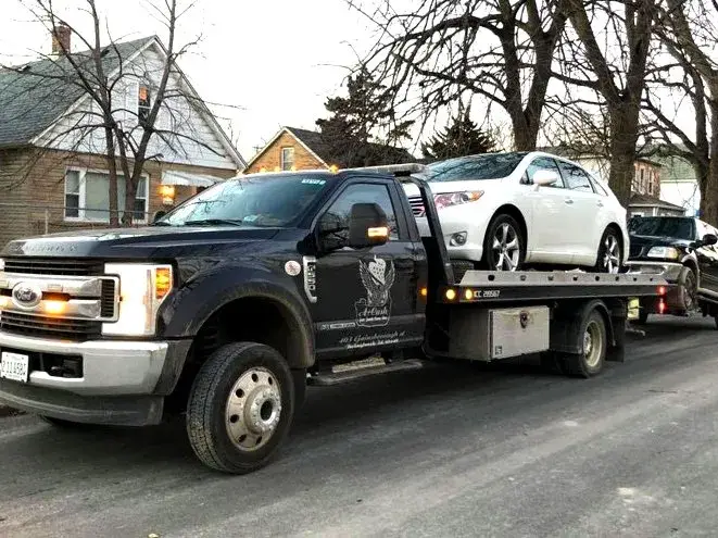 Tow truck on the street towing away two junk cars that is white and black