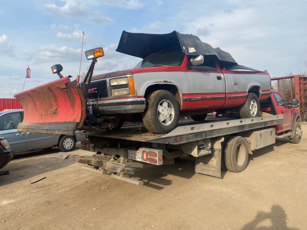 Tow truck on the junk yard towing away a stripe red-gray junk car