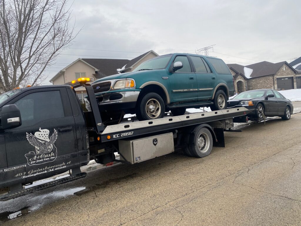 Tow truck on the street towing away a blue junk car
