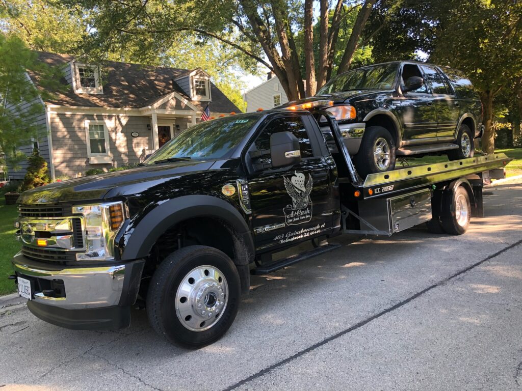 Tow truck on the street towing away a black junk car