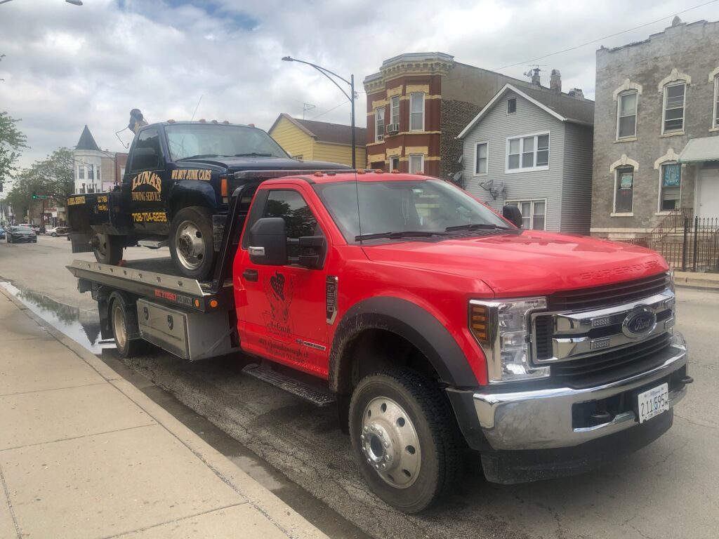 Tow truck on the street towing away a black junk car