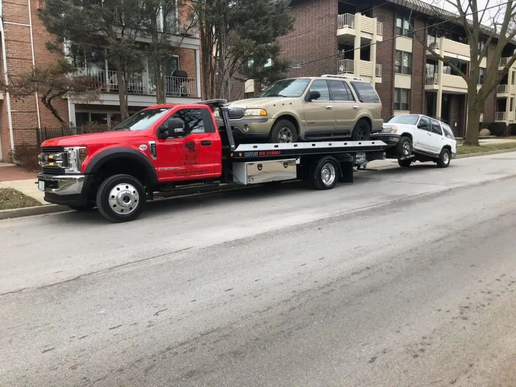 Tow truck on the street towing away a gray junk car