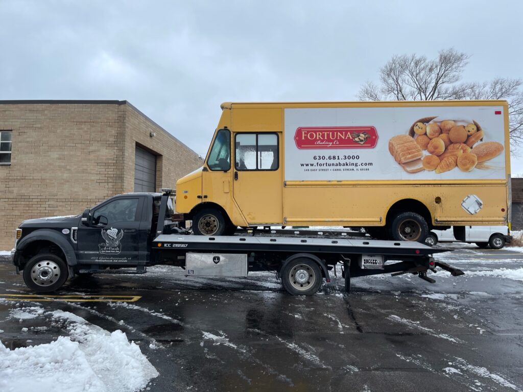 Tow truck on the street towing away a yellow junk van