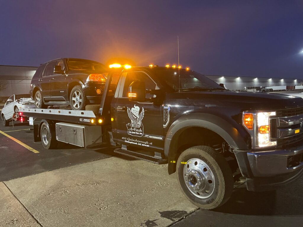 Tow truck on the street towing away a black junk car