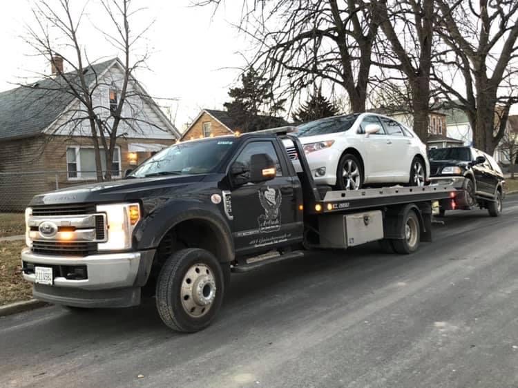Tow truck on the street towing away a white junk car
