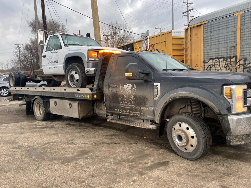 Tow truck on the street towing away a white junk car