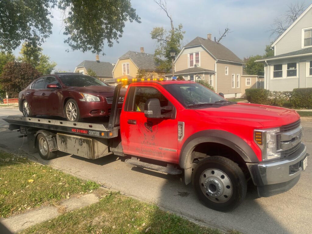 Tow truck on the street towing away a maroon junk car
