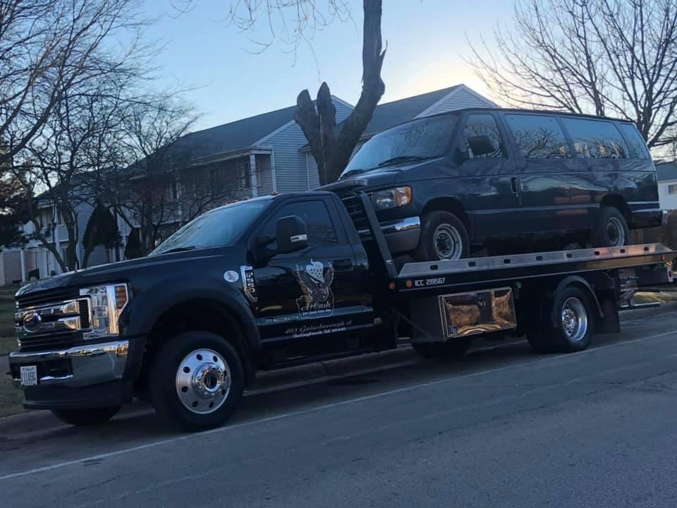 A junk car on the flatbed of a truck from A+ Junk and Tow on the street of Oak Brook IL