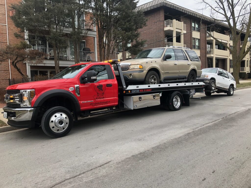 A tow truck on the street towing away a gray junk car.