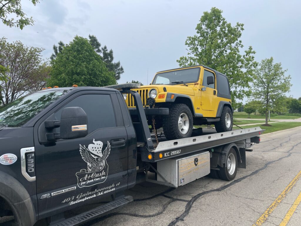A tow truck on the street towing away a yellow jeep.