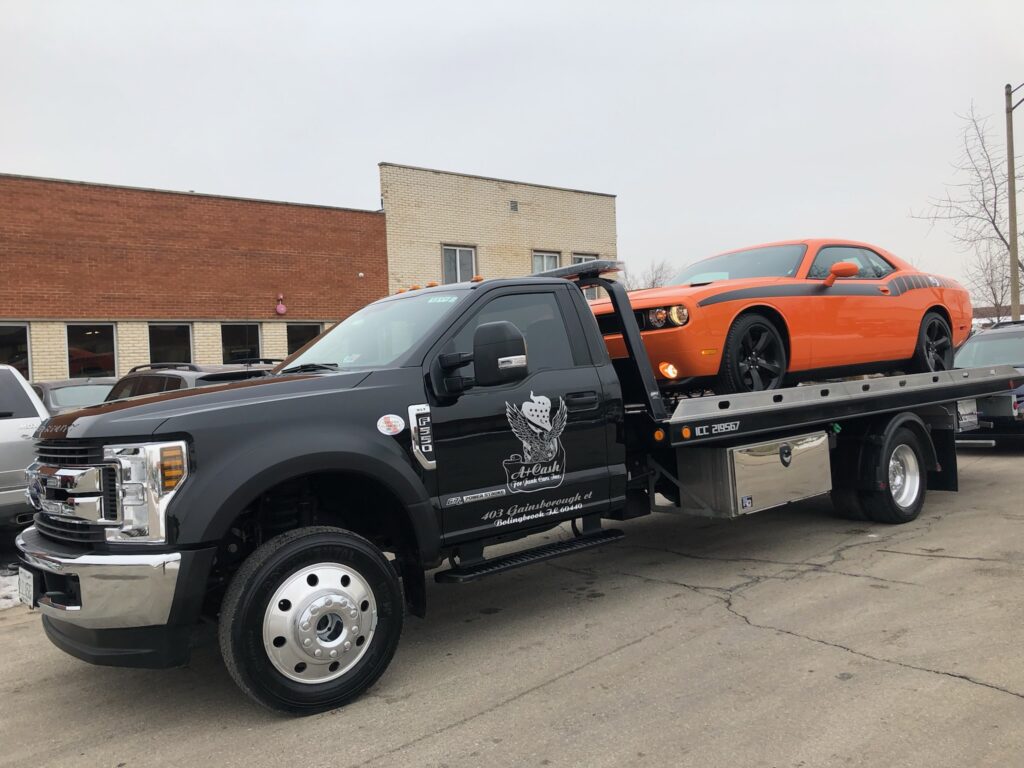 A junk car on the flatbed of a truck from A+ Junk and Tow on the street of Orland Hills IL