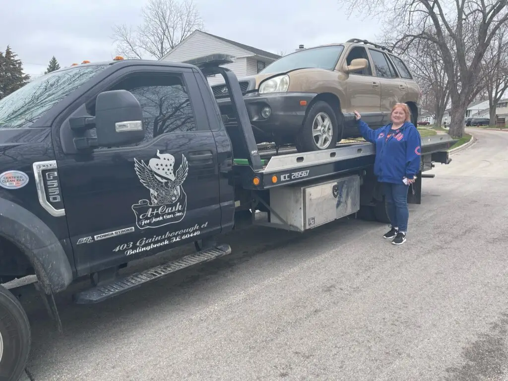 A junk car on the flatbed of a truck from A+ Junk and Tow on the street of Plainfield IL