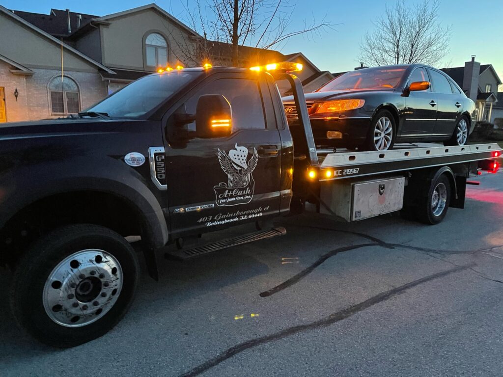 A tow truck on the street towing away a black junk car.