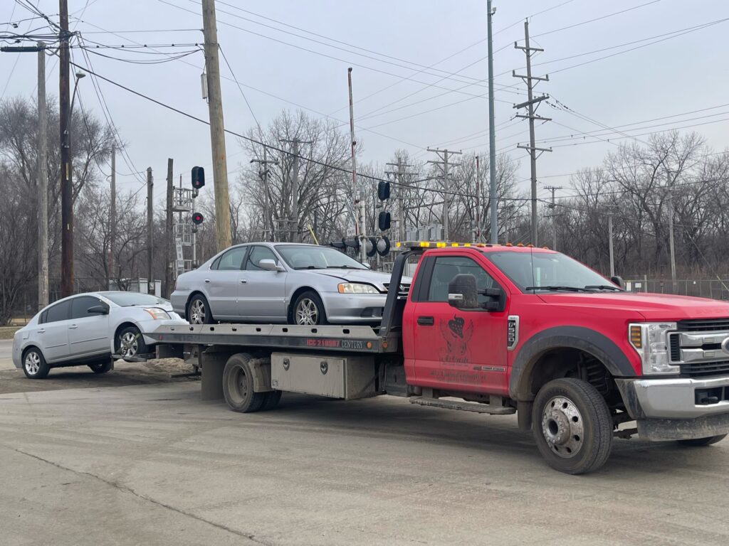 A junk car on the flatbed of a truck from A+ Junk and Tow on the street of Shorewood IL