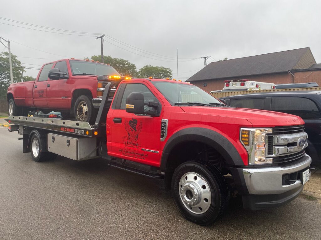 A tow truck on the street towing away a red junk car