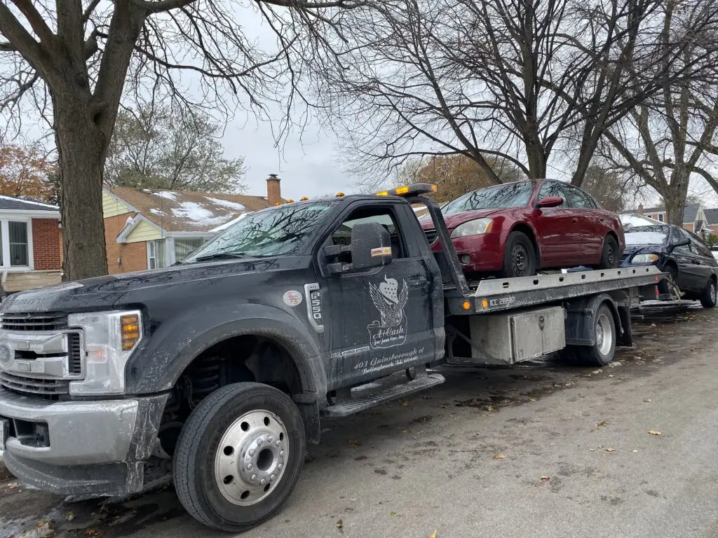 A junk car on the flatbed of a truck from A+ Junk and Tow on the street of Westmont IL