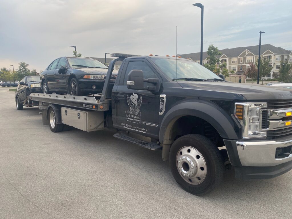 A junk car on the flatbed of a truck from A+ Junk and Tow on the street of Westmont IL