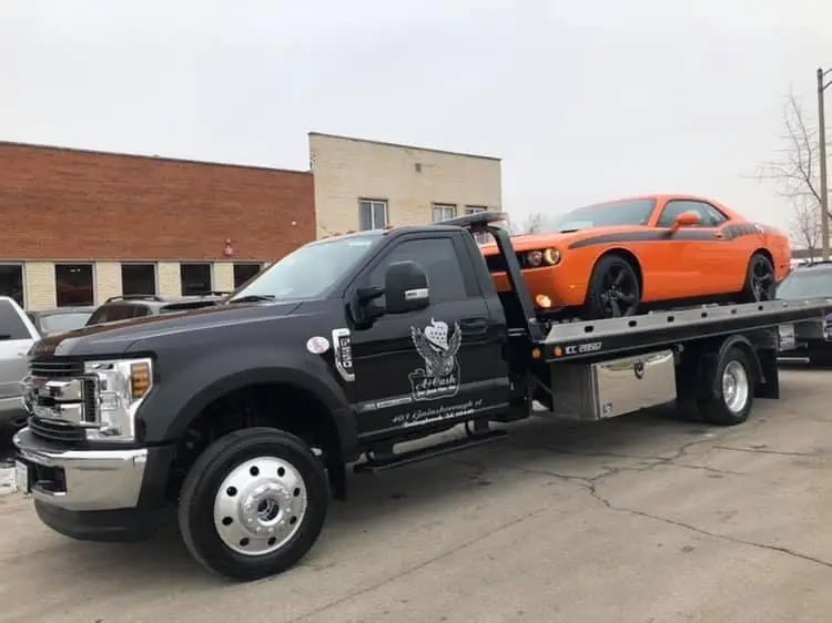 A tow truck on the street towing away a orange junk car
