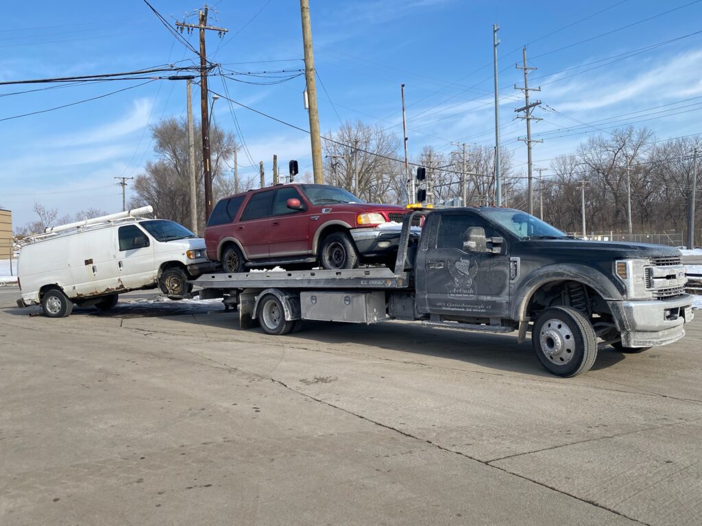 A junk car on the flatbed of a truck from A+ Junk and Tow on the street of Willowbrook IL