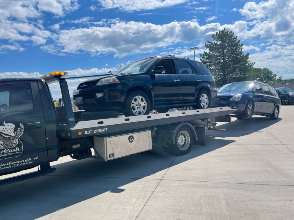 A junk car on the flatbed of a truck from A+ Junk and Tow on the street of Winfield IL