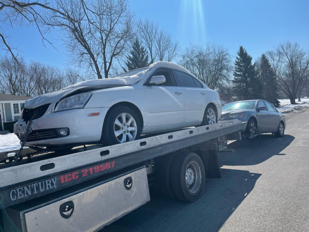 A junk car on the flatbed of a truck from A+ Junk and Tow on the street of Winfield IL