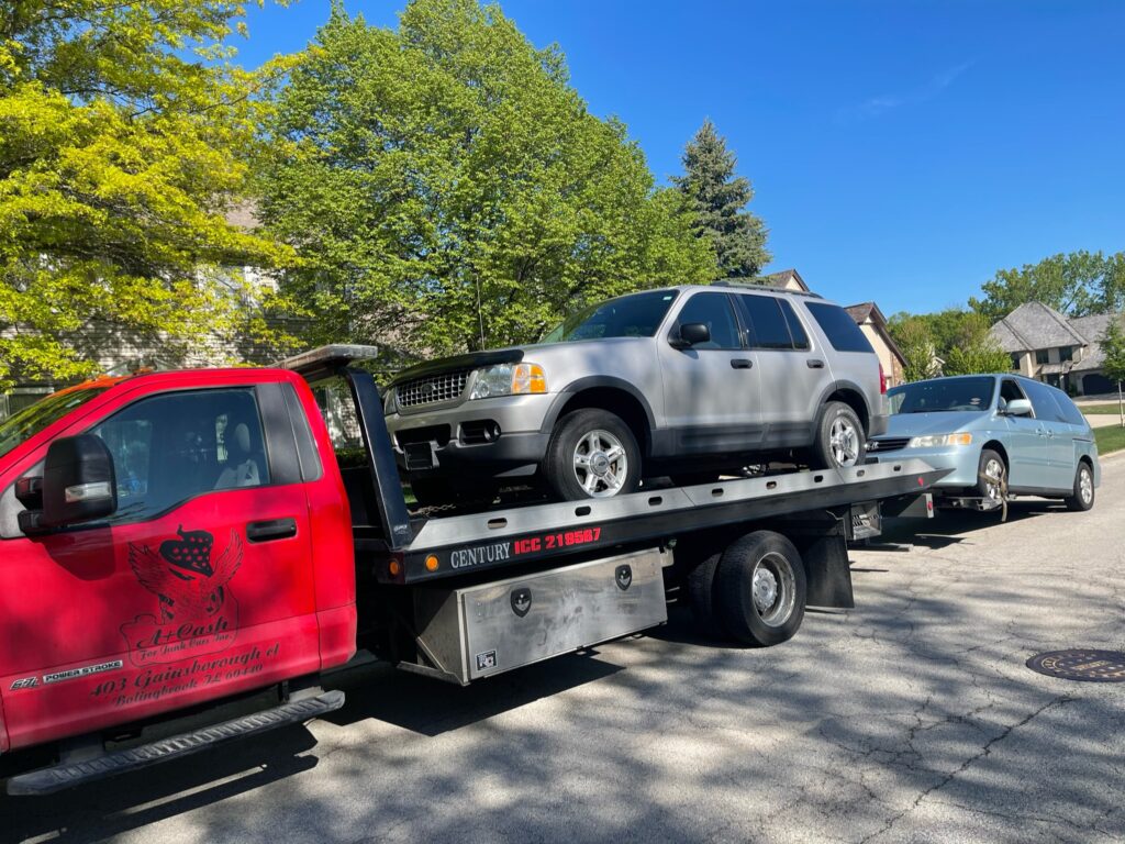 A junk car on the flatbed of a truck from A+ Junk and Tow on the street of Winfield IL
