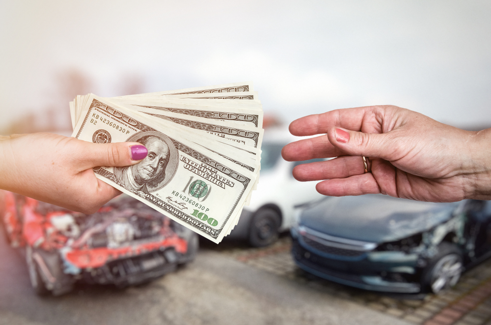 Person handing cash to another for junk cars sale, with damaged vehicles in the background, Lemont, IL