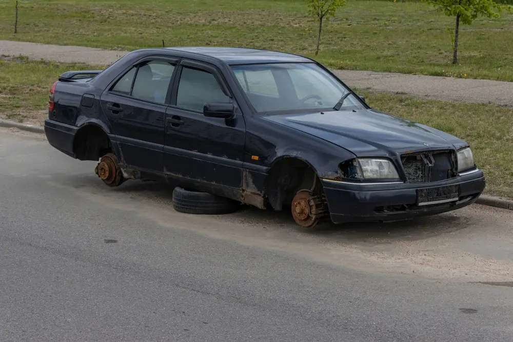 a dark blue car with out wheels on the street waiting for a tow truck