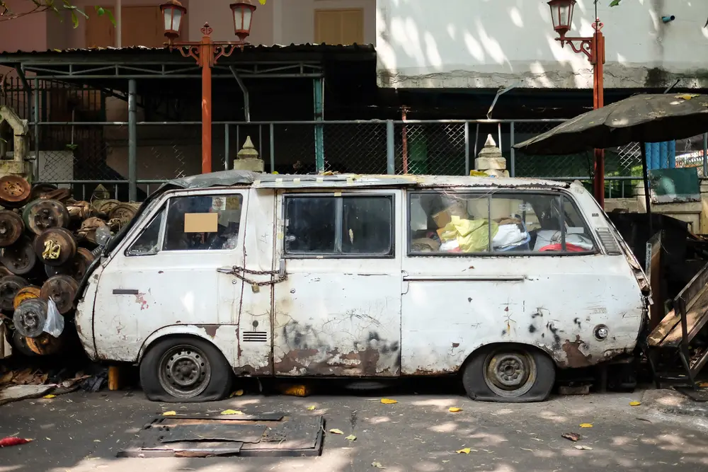 A rusty old white van in a junk with a flat tires