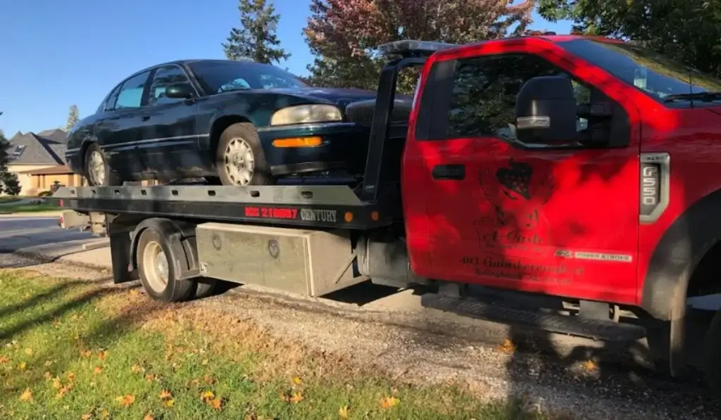 Tow truck hauls away old sedan during junk car selling process in Joliet, IL residential neighborhood.
