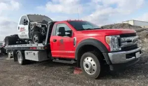 Tow truck transporting severely damaged wrecked vehicle to salvage yard, showing fast cash solutions for unusable cars.