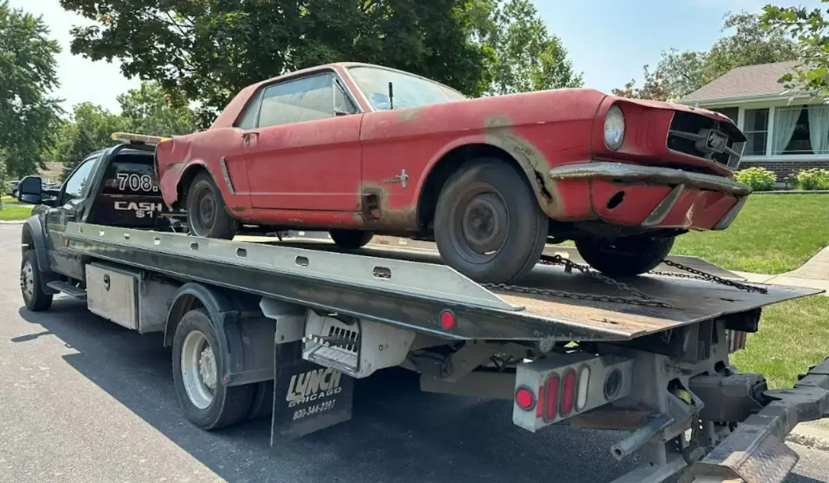 Rusty red junk car being professionally towed from a suburban Bolingbrook driveway by removal service truck.