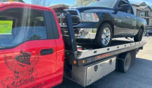 Red tow truck from A+ Cash For Junk Cars hauling a black junk car without title.