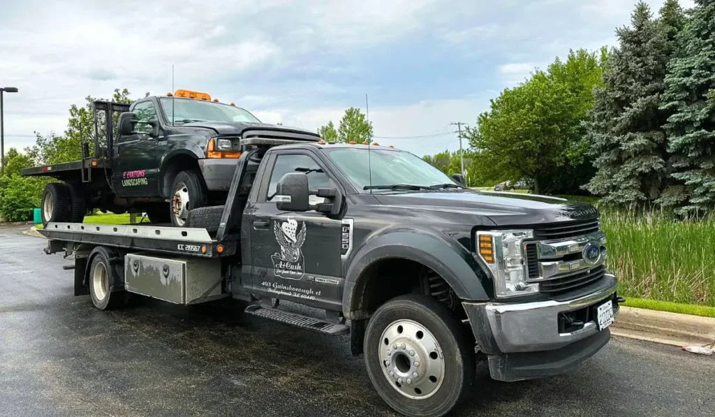 Tow truck hauling old landscaping truck after Sell Your Junk Truck request in Plainfield summer pickup service.