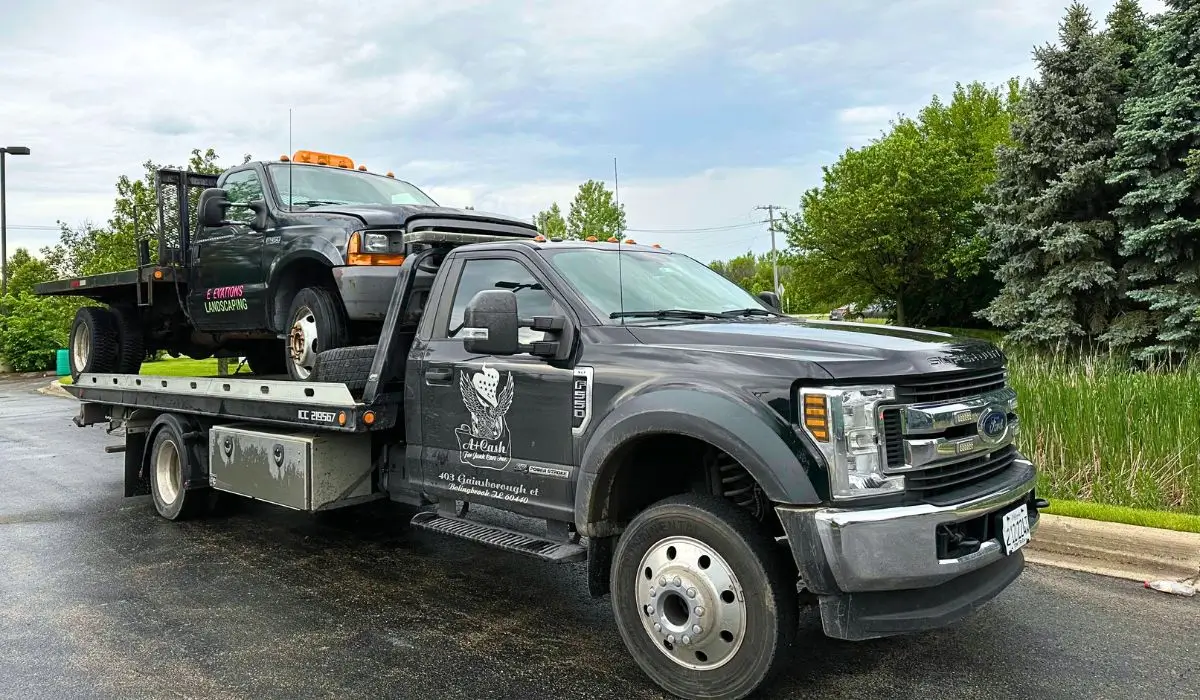 Tow truck hauling old landscaping truck after Sell Your Junk Truck request in Plainfield summer pickup service.