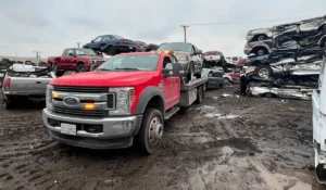 A red tow truck transporting a car junked in Lemont, IL to a salvage yard where vehicles are stacked for recycling.