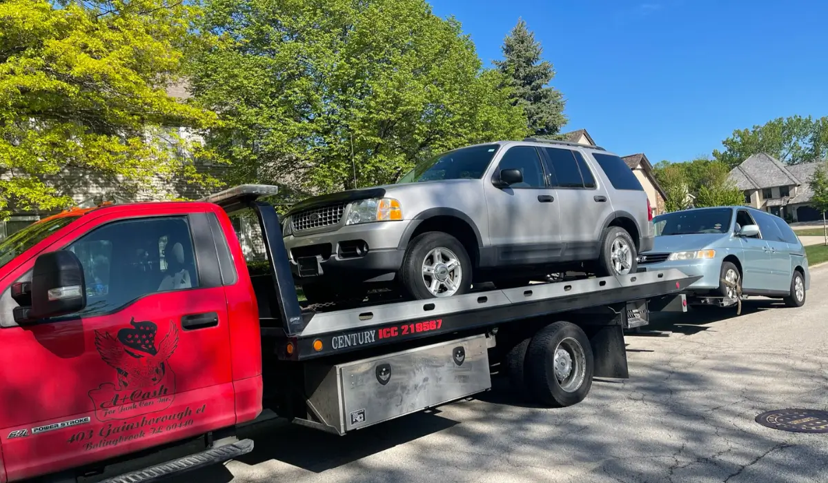 Tow truck removing multiple junk cars in Joliet IL from a residential street during daytime pickup service.