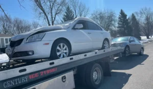 Damaged snow-covered vehicle being towed on flatbed during best time to junk your car in Lemont.