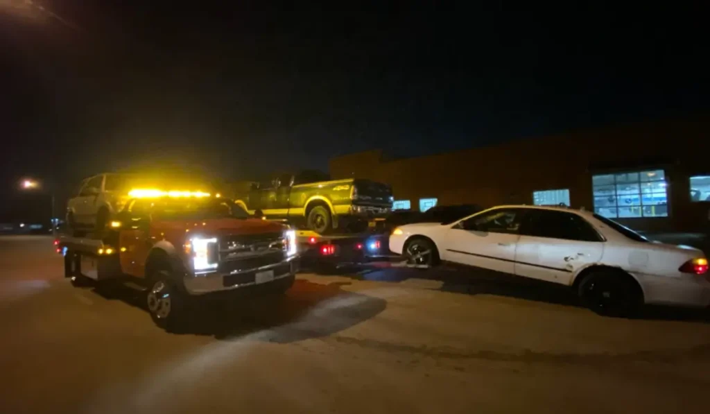 Tow truck hauling abandoned car at night in Homer Glen for legal junk vehicle removal service.